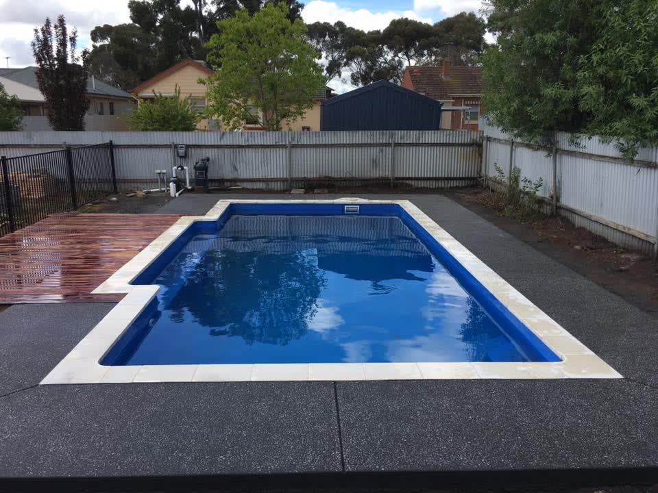 An in-ground pool edged in exposed-aggregate concrete, with a timber deck running alongside